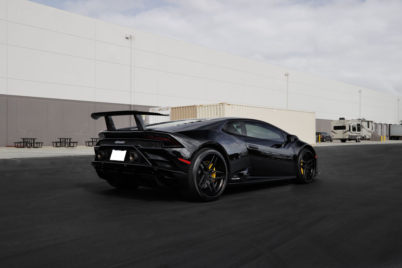 Black Lamborghini Huracán with rear wing parked outside a warehouse