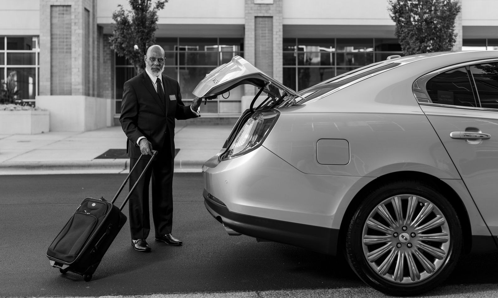 Chauffeur in suit loading luggage into luxury car trunk