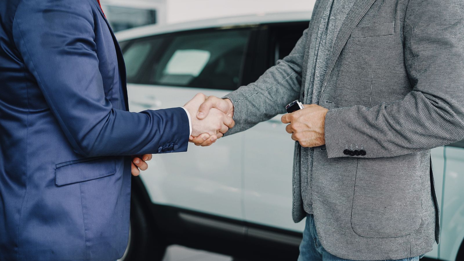 Two businessmen shaking hands in a car dealership