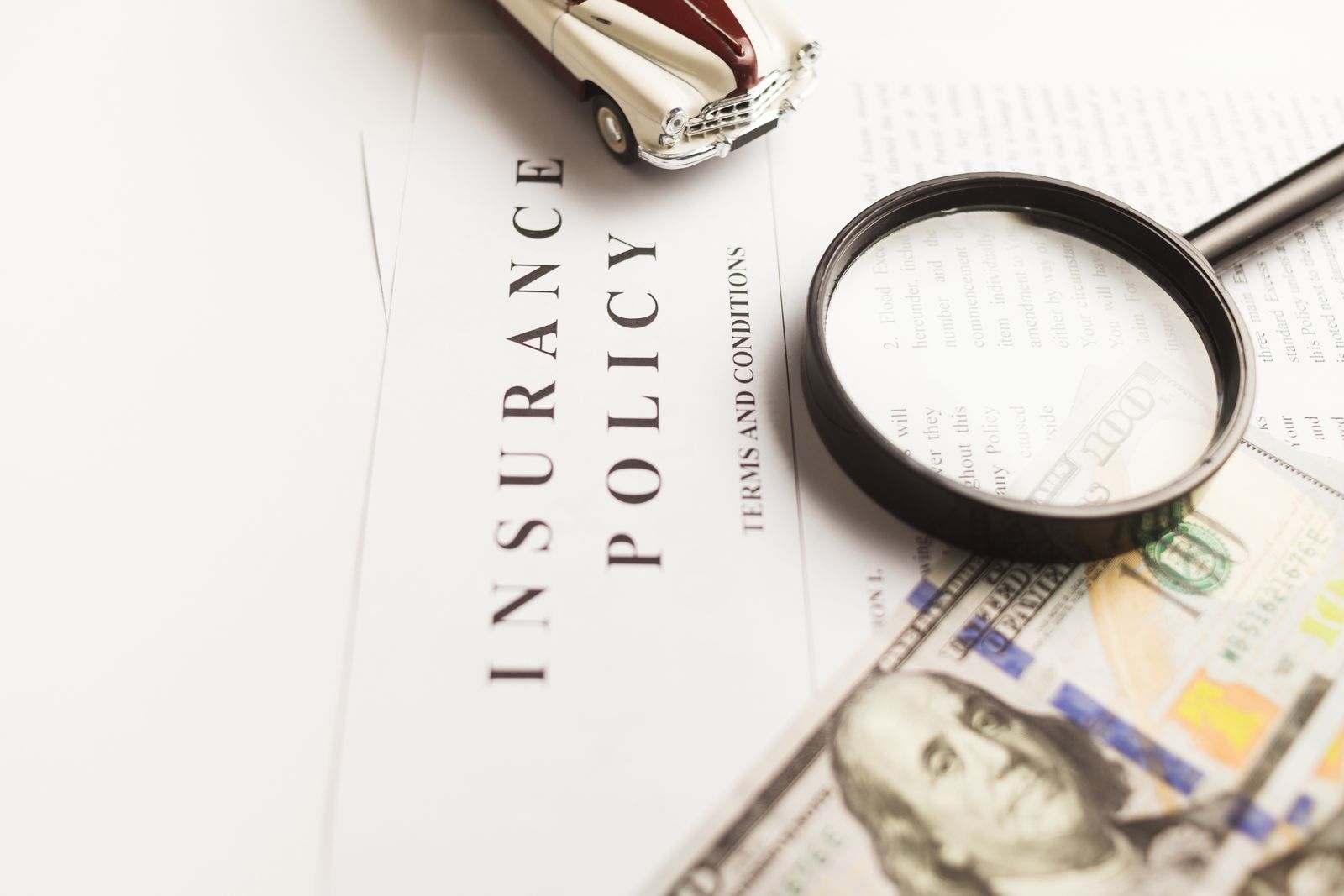 Insurance policy with magnifying glass, money, and toy car