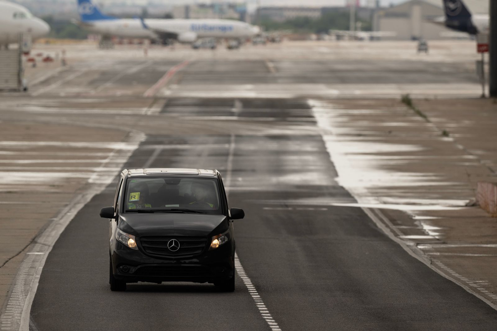 Black van driving on a rainy airport runway