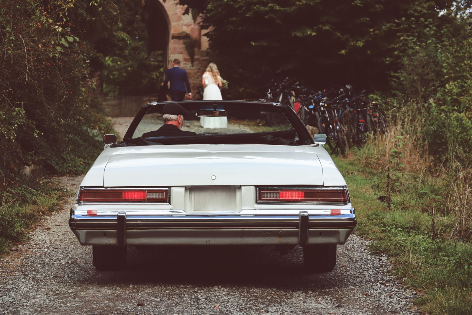 Vintage car parked on a gravel path with bride and groom walking ahead